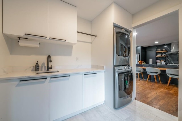 kitchen featuring white cabinetry, sink, stacked washer / drying machine, light stone countertops, and light hardwood / wood-style flooring