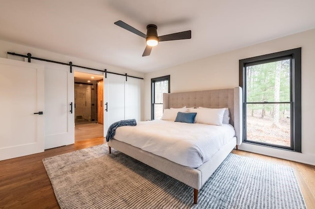 bedroom with multiple windows, a barn door, hardwood / wood-style floors, and ceiling fan