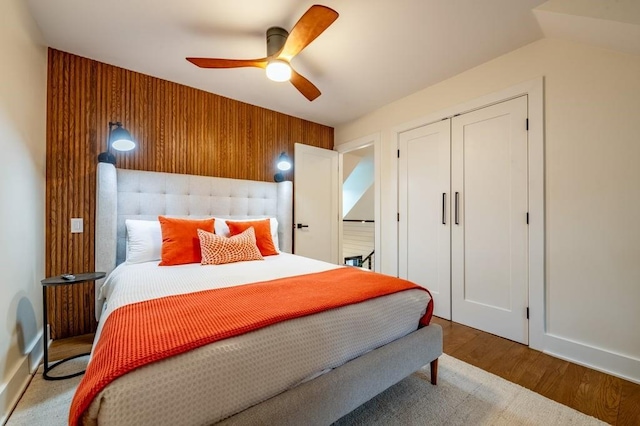 bedroom with a closet, wood-type flooring, wooden walls, and ceiling fan