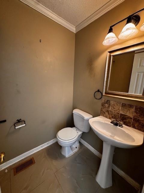 half bath with baseboards, visible vents, a textured ceiling, crown molding, and toilet