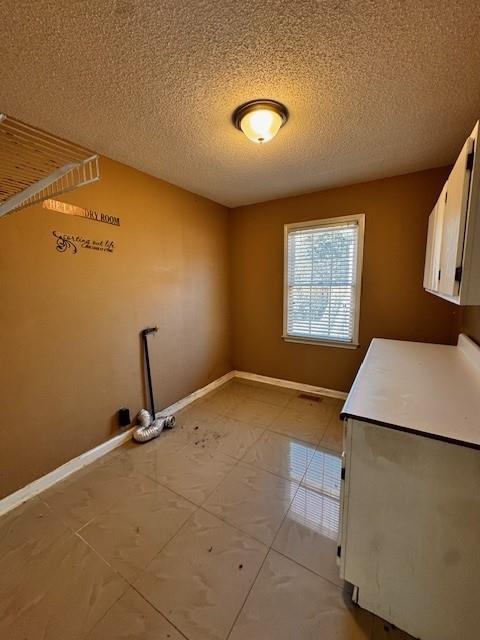 washroom with cabinet space, a textured ceiling, and baseboards