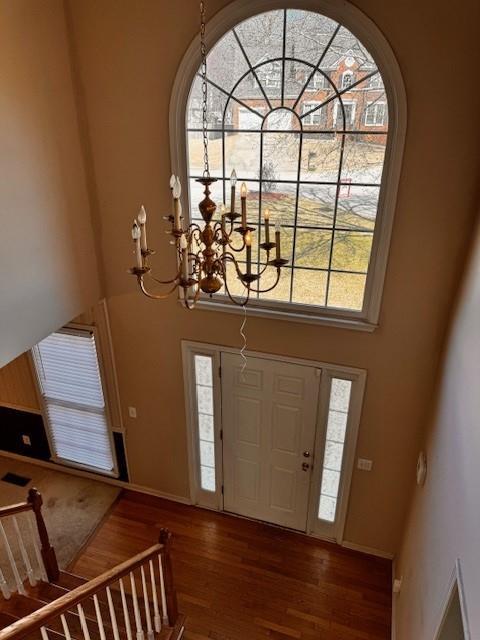 foyer entrance with baseboards, a notable chandelier, a high ceiling, and wood finished floors