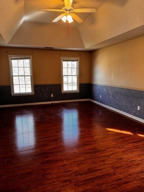 empty room with dark wood-type flooring, ceiling fan, a wainscoted wall, lofted ceiling, and a raised ceiling