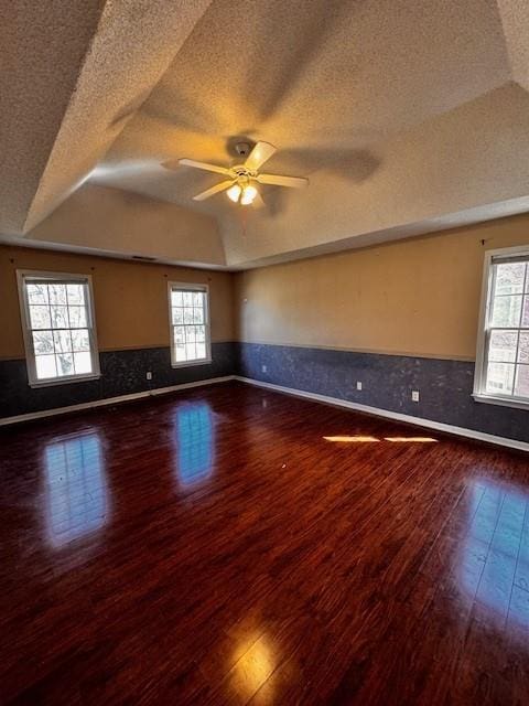 empty room featuring a tray ceiling, hardwood / wood-style flooring, plenty of natural light, and wainscoting