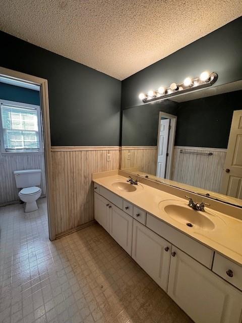 full bathroom featuring a sink, a wainscoted wall, toilet, and a textured ceiling