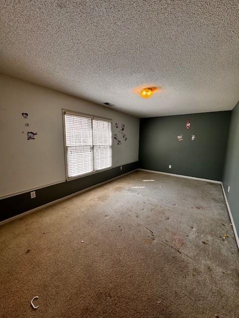 carpeted empty room featuring visible vents, baseboards, and a textured ceiling