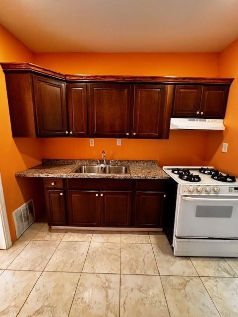 kitchen featuring visible vents, white range with gas stovetop, a sink, dark brown cabinets, and under cabinet range hood