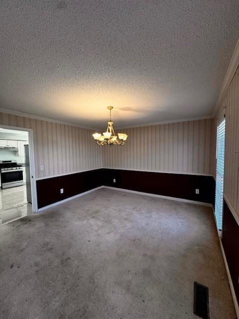 empty room with carpet floors, a textured ceiling, a chandelier, and ornamental molding