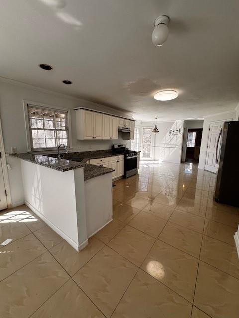 kitchen with a peninsula, dark stone counters, stainless steel range with gas stovetop, freestanding refrigerator, and ornamental molding