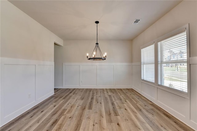 unfurnished dining area with an inviting chandelier and light wood-type flooring