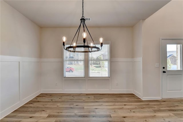 unfurnished dining area with light wood-type flooring, plenty of natural light, and an inviting chandelier