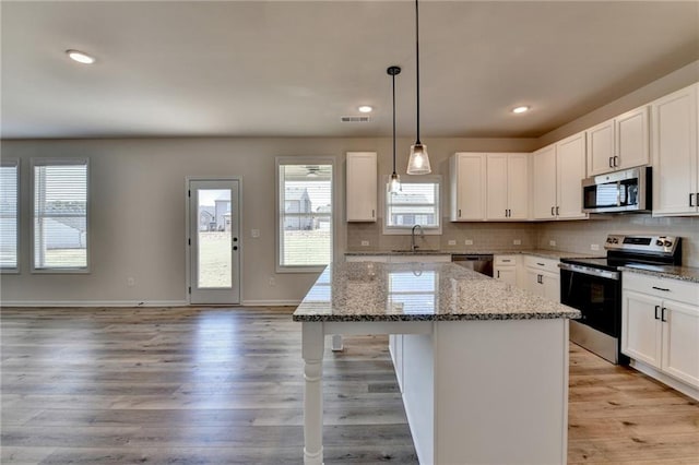 kitchen with a kitchen island, white cabinets, light stone counters, and stainless steel appliances