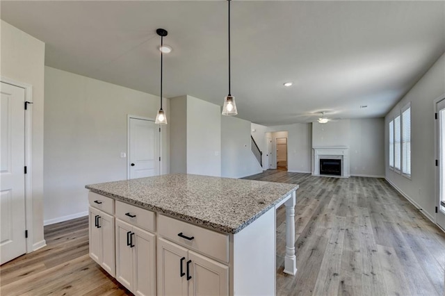 kitchen with a kitchen island, white cabinetry, light wood-type flooring, light stone countertops, and hanging light fixtures