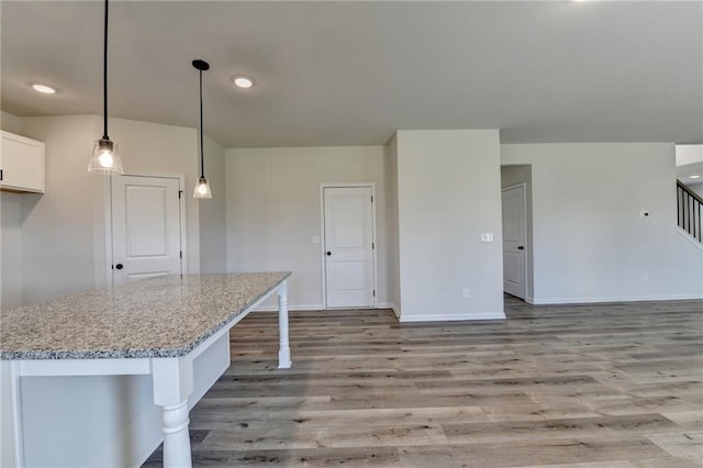 kitchen featuring decorative light fixtures, light stone countertops, a kitchen breakfast bar, white cabinets, and light hardwood / wood-style flooring