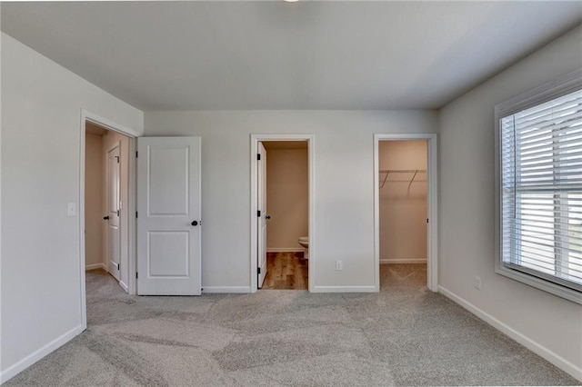 unfurnished bedroom featuring ensuite bath, light colored carpet, multiple windows, and a walk in closet