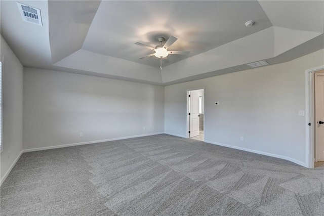 empty room featuring ceiling fan, light carpet, and a raised ceiling