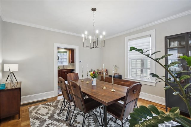 dining room with a notable chandelier, ornamental molding, light parquet flooring, and sink