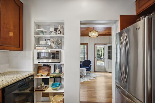 kitchen with appliances with stainless steel finishes, light hardwood / wood-style flooring, backsplash, light stone countertops, and a notable chandelier