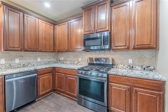 kitchen featuring stainless steel appliances, light stone counters, dark wood finished floors, and tasteful backsplash