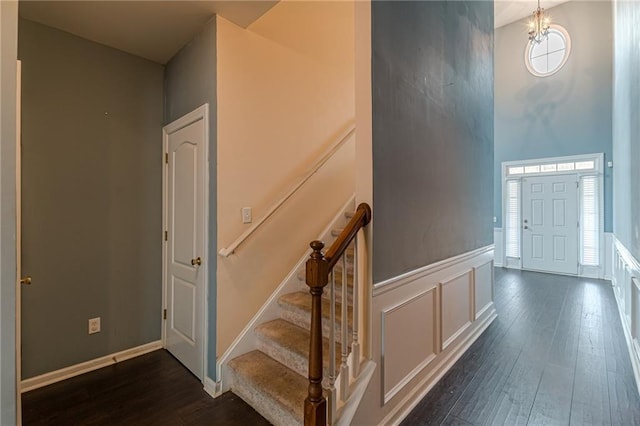 foyer entrance featuring a decorative wall, a wainscoted wall, dark wood-style flooring, a towering ceiling, and stairs