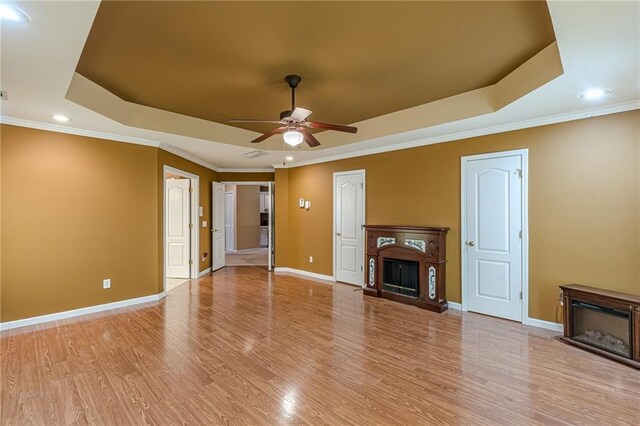 unfurnished living room featuring light wood-type flooring, a raised ceiling, ceiling fan, and crown molding