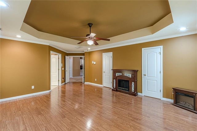 unfurnished living room with ceiling fan, a fireplace, baseboards, light wood-type flooring, and a raised ceiling