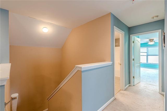 corridor with vaulted ceiling, baseboards, light colored carpet, and an upstairs landing