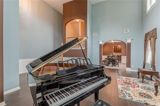 sitting room featuring baseboards, visible vents, arched walkways, a towering ceiling, and wood finished floors