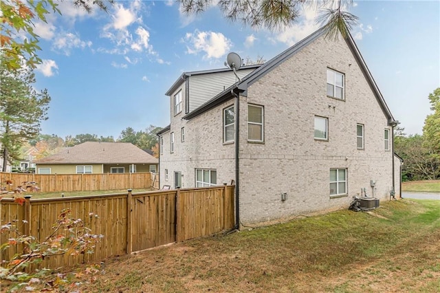 back of property with a yard, central AC, brick siding, and fence