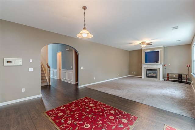 living area with a fireplace with flush hearth, arched walkways, ceiling fan, and wood finished floors