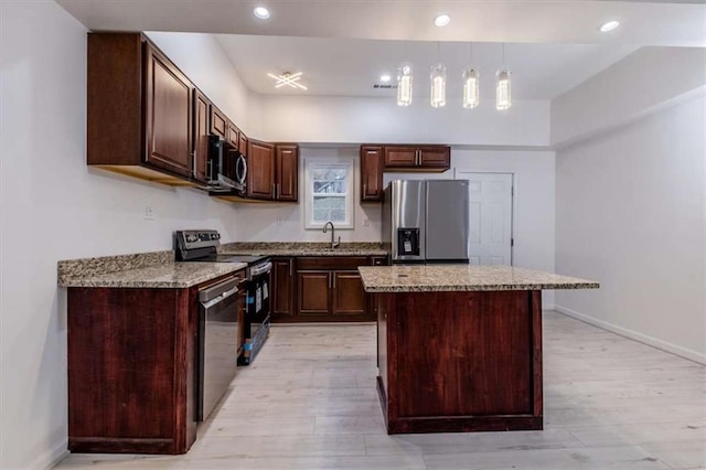 kitchen featuring light wood-type flooring, light stone countertops, appliances with stainless steel finishes, and a center island