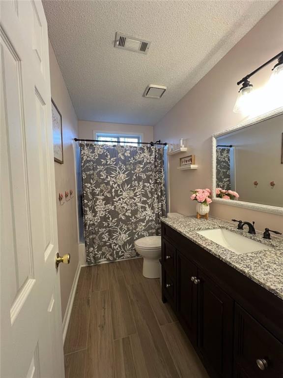 full bathroom with toilet, shower / bath combination with curtain, a textured ceiling, vanity, and hardwood / wood-style flooring