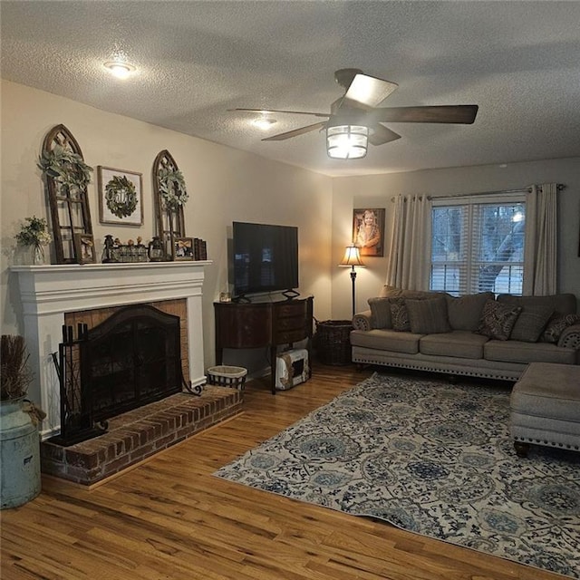 living room with ceiling fan, hardwood / wood-style floors, a brick fireplace, and a textured ceiling