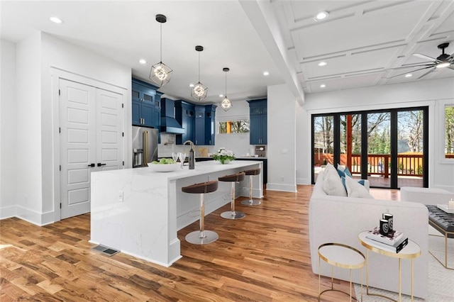 kitchen featuring stainless steel fridge with ice dispenser, a breakfast bar area, blue cabinets, and wall chimney range hood