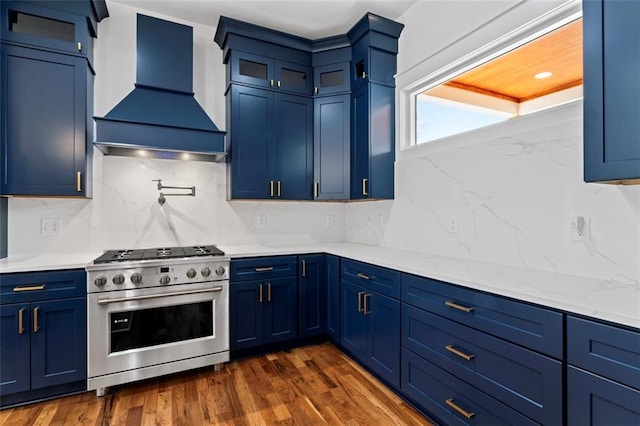 kitchen featuring high end stove, blue cabinetry, glass insert cabinets, custom exhaust hood, and dark wood-style flooring