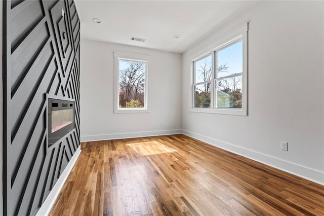 unfurnished room featuring wood-type flooring, visible vents, baseboards, and a wealth of natural light