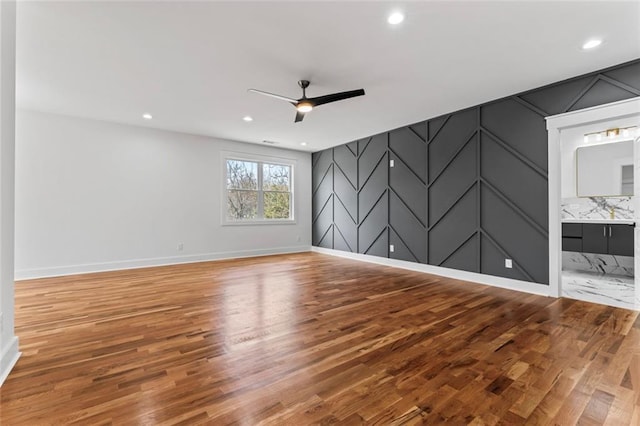 empty room with an accent wall, a ceiling fan, wood finished floors, a decorative wall, and recessed lighting