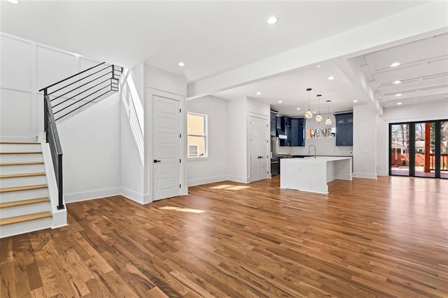 unfurnished living room featuring plenty of natural light, recessed lighting, stairs, and wood finished floors
