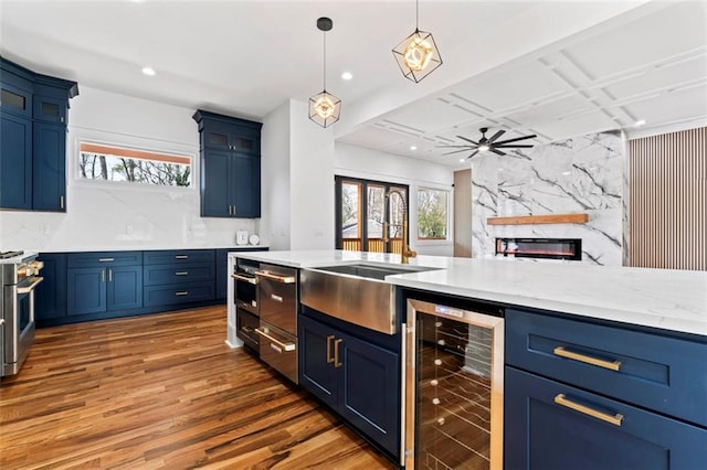 kitchen featuring range with two ovens, a ceiling fan, wood finished floors, blue cabinets, and beverage cooler