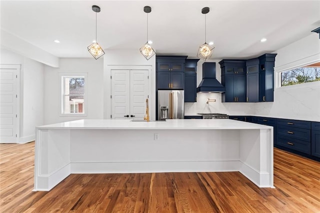 kitchen with light countertops, stainless steel fridge, custom exhaust hood, a sink, and blue cabinets