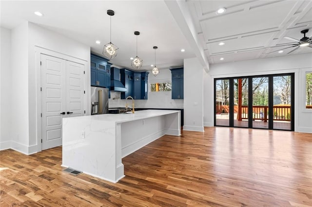 kitchen with light wood-style flooring, blue cabinets, wall chimney exhaust hood, and high end refrigerator