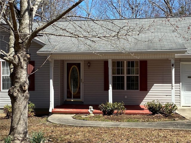 property entrance featuring a garage, covered porch, and a shingled roof