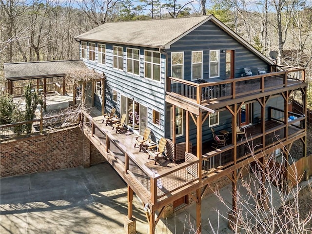 rear view of house with a deck, a patio, and a shingled roof