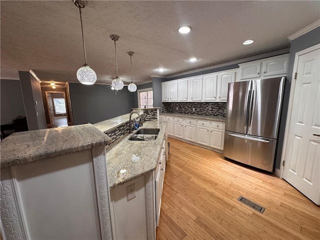 kitchen featuring stainless steel fridge, sink, light hardwood / wood-style floors, white cabinetry, and hanging light fixtures