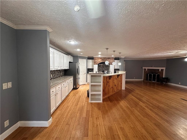 kitchen with stainless steel fridge, a center island with sink, white cabinetry, and light hardwood / wood-style floors