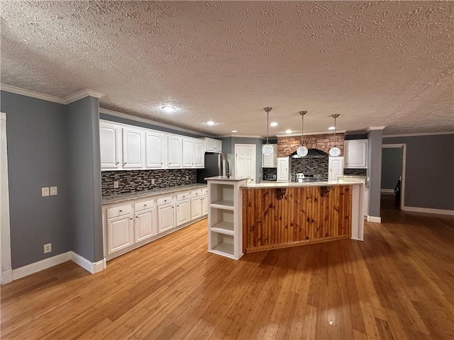 kitchen with white cabinets, a large island with sink, light wood-type flooring, and decorative light fixtures