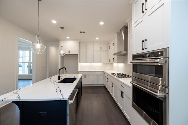 kitchen featuring white cabinetry, sink, stainless steel appliances, wall chimney range hood, and an island with sink