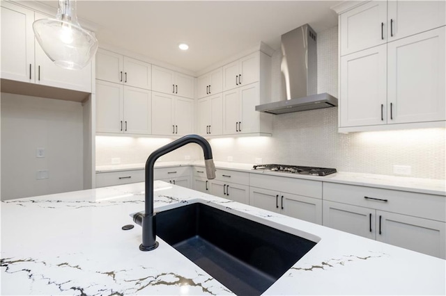 kitchen featuring stainless steel gas cooktop, sink, wall chimney range hood, pendant lighting, and white cabinets