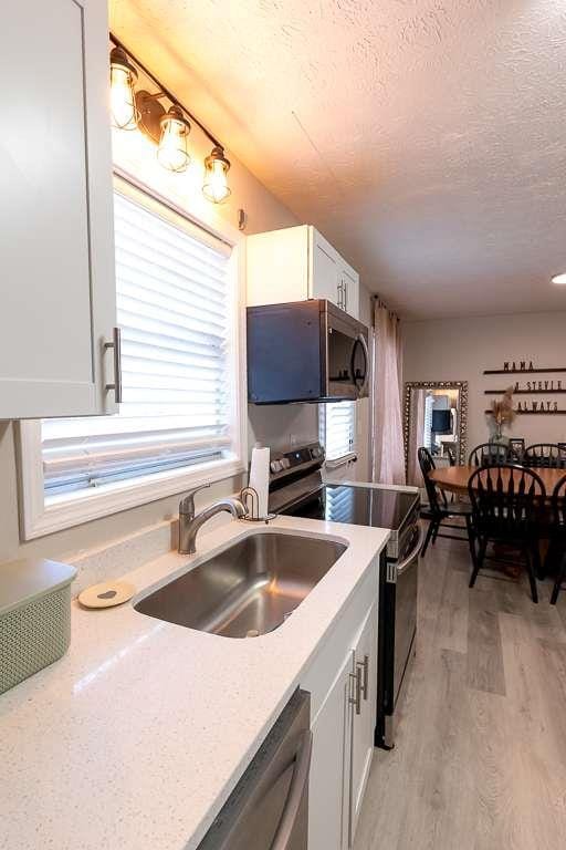 kitchen with sink, white cabinets, light hardwood / wood-style floors, stainless steel appliances, and a textured ceiling