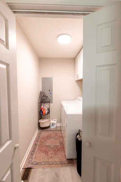 clothes washing area with independent washer and dryer, electric panel, cabinets, and light wood-type flooring